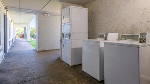A laundry area with stacked washers and dryers, a concrete floor, and a hallway leading to an outdoor area. - Motel 6 Stockbridge, GA – Hwy 138 W (Stockbridge)