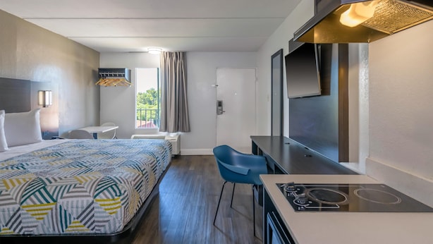 A hotel room with a bed, a desk with a stove, a chair, a TV, and a window with curtains. - Motel 6 Stockbridge, GA – Hwy 138 W (Stockbridge)