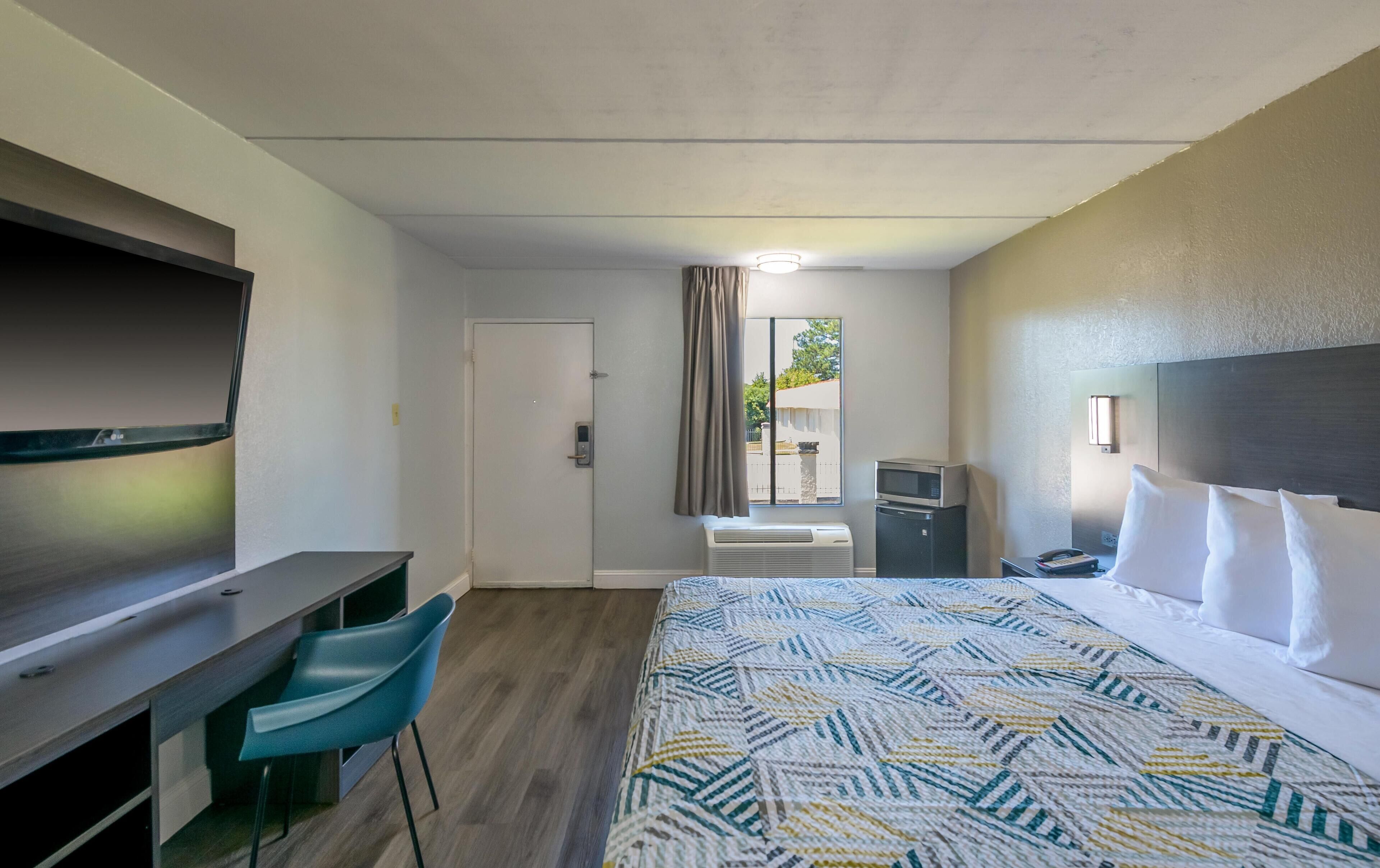 A hotel room with a bed, a desk, a chair, a microwave, and a TV.