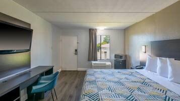 A hotel room with a bed, a desk, a chair, a microwave, and a TV.