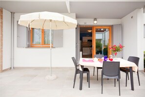 Un espace repas comprenant une table, des chaises et un parasol blanc.