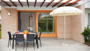 An outdoor patio with a table set for dining, a white umbrella, and a brick wall. - Villaggio Laguna Blu (Caorle)