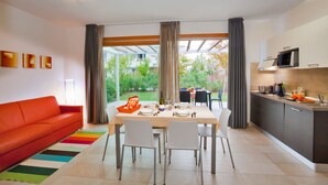 A modern kitchen with a dining area, featuring a large window, a sofa, and a colorful rug. - Villaggio Laguna Blu (Caorle)