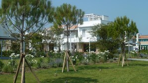 A modern building with a flat roof and white exterior walls, surrounded by a well-maintained garden with various plants and flowers. - Villaggio Laguna Blu (Caorle)