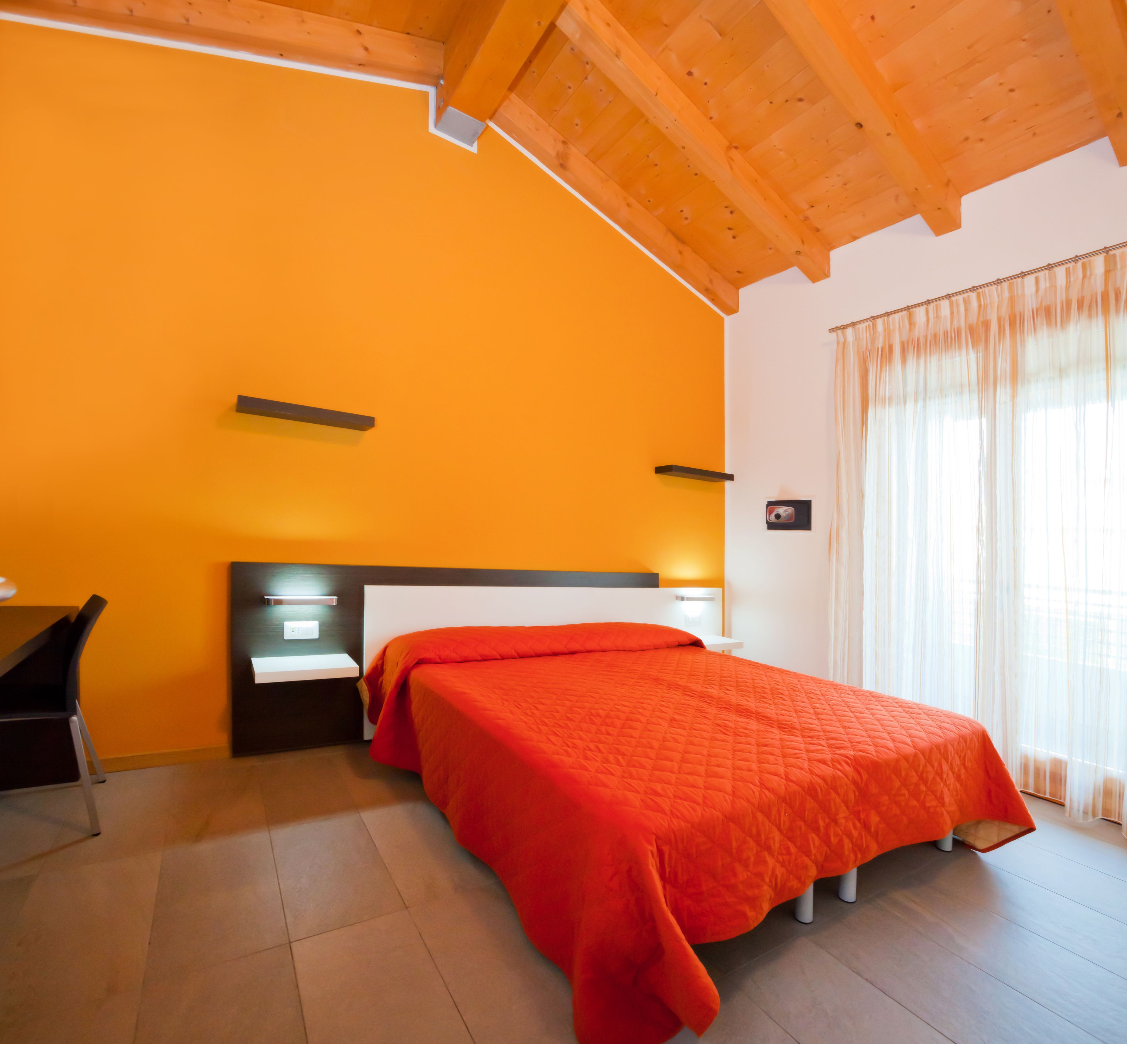 A bedroom with a bed, bedside tables, a desk, and a window with curtains.
