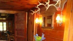 A wooden interior with a patterned rug, a table with a vase of flowers, and a ceiling with antler decorations. - Chestnut Lodge (Lee)