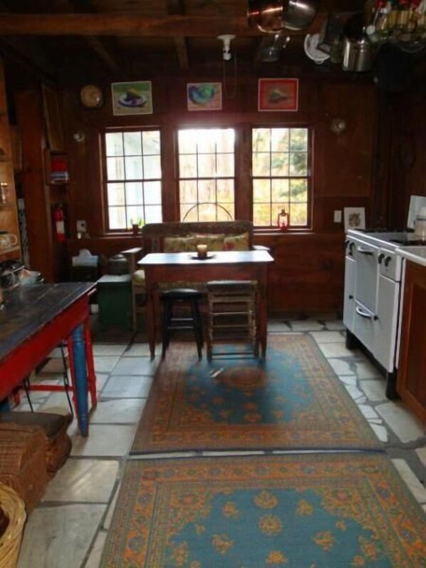 A rustic kitchen with wooden walls, a dining table, chairs, and a stove.