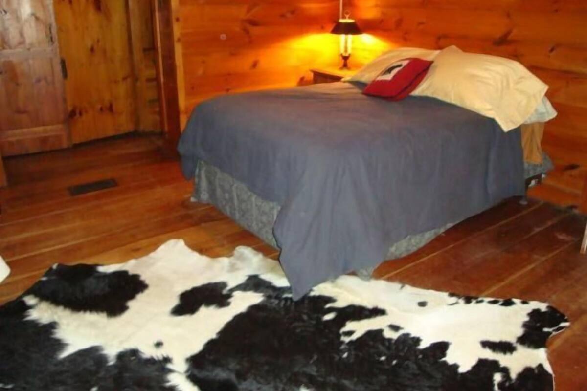 A wooden cabin room with a bed, a nightstand, and a cowhide rug.