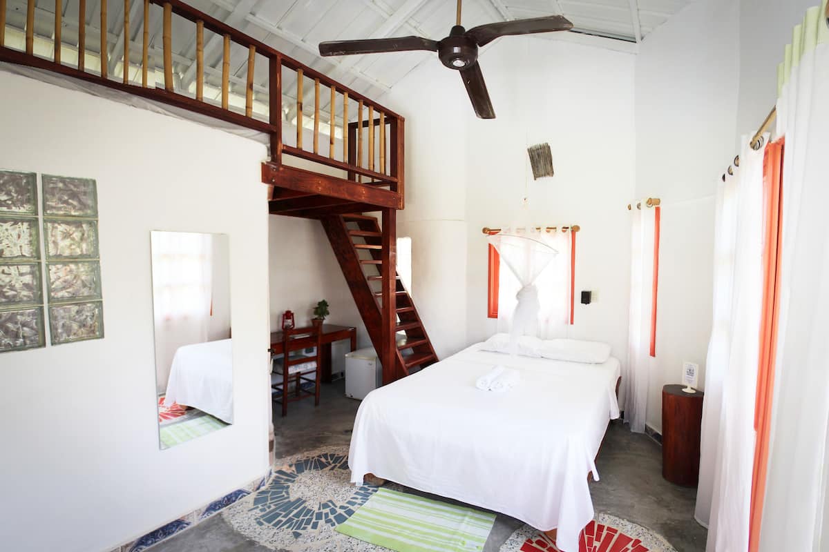 Une chambre avec un grand lit, un escalier en bois, un ventilateur de plafond et un petit bureau avec une chaise.