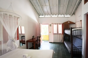 A room with a bed, a desk, a chair, a mosquito net, a bunk bed, and a door leading to an outdoor area.