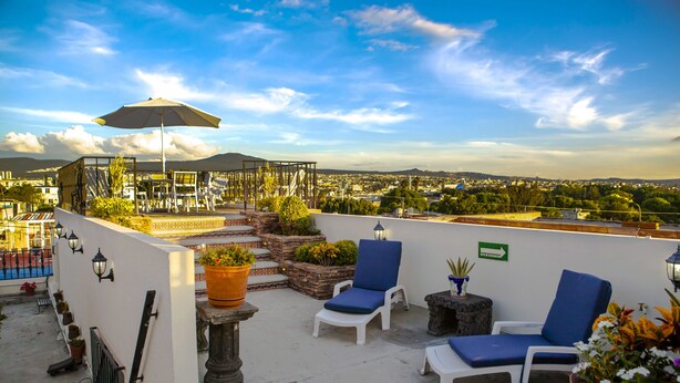 Terraza en la azotea con sillones de descanso, plantas en macetas y vistas a la ciudad.