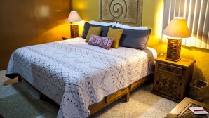 Una cama bien hecha con un edredón estampado, dos lámparas de noche y un adorno de pared decorativo.
