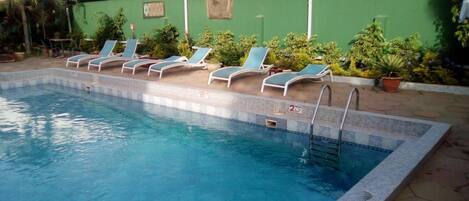A swimming pool with lounge chairs and a green wall.