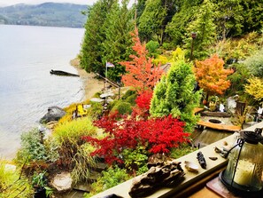 Un jardín junto al lago con diversos árboles, una terraza de madera y un farol.