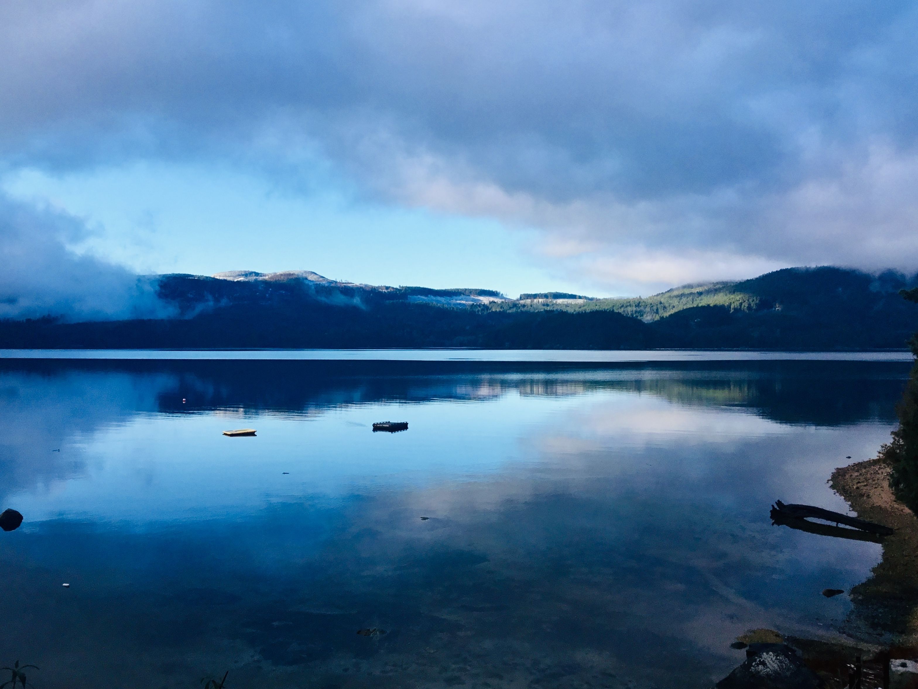 A calm lake with a clear reflection of the sky and distant mountains.