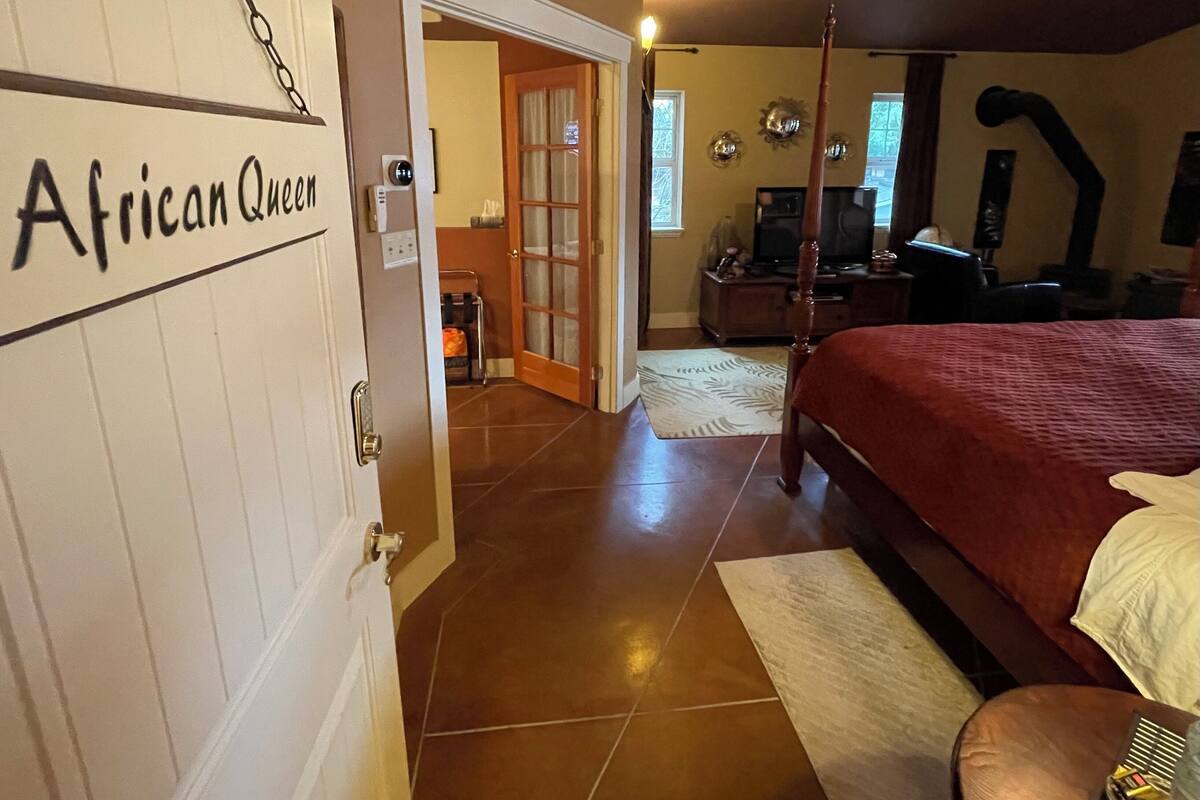 A bedroom with a bed, a wooden door labeled 'African Queen,' a television, and a fireplace.