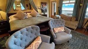 A bedroom with a bed, two armchairs, a chandelier, a painting, and a view of the outdoors. - The Tuwanek Hotel and Spa (Sechelt)