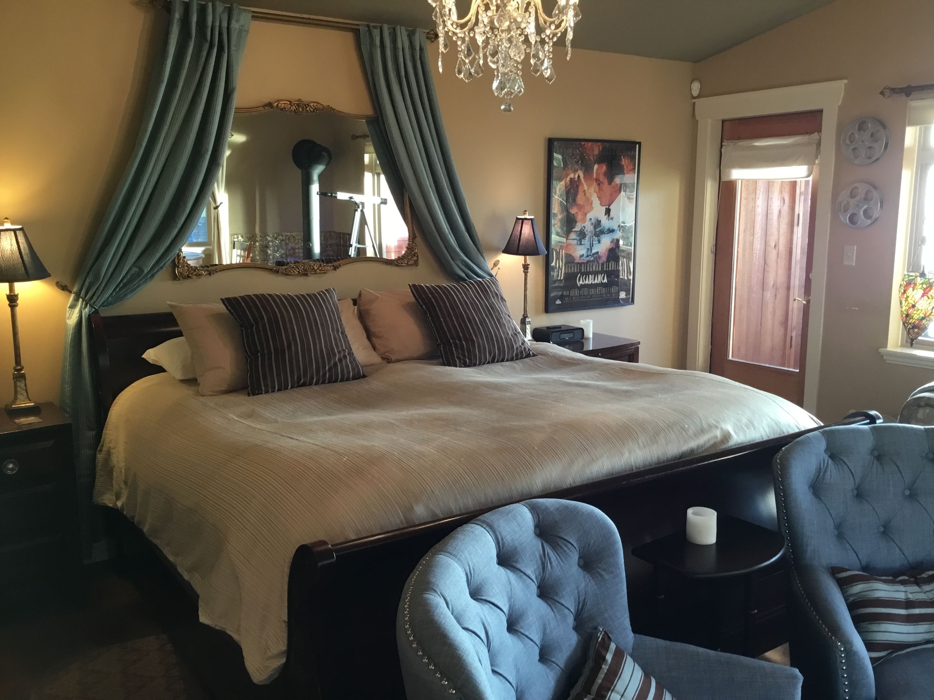 A bedroom with a large bed, a chandelier, a mirror, and a poster on the wall.