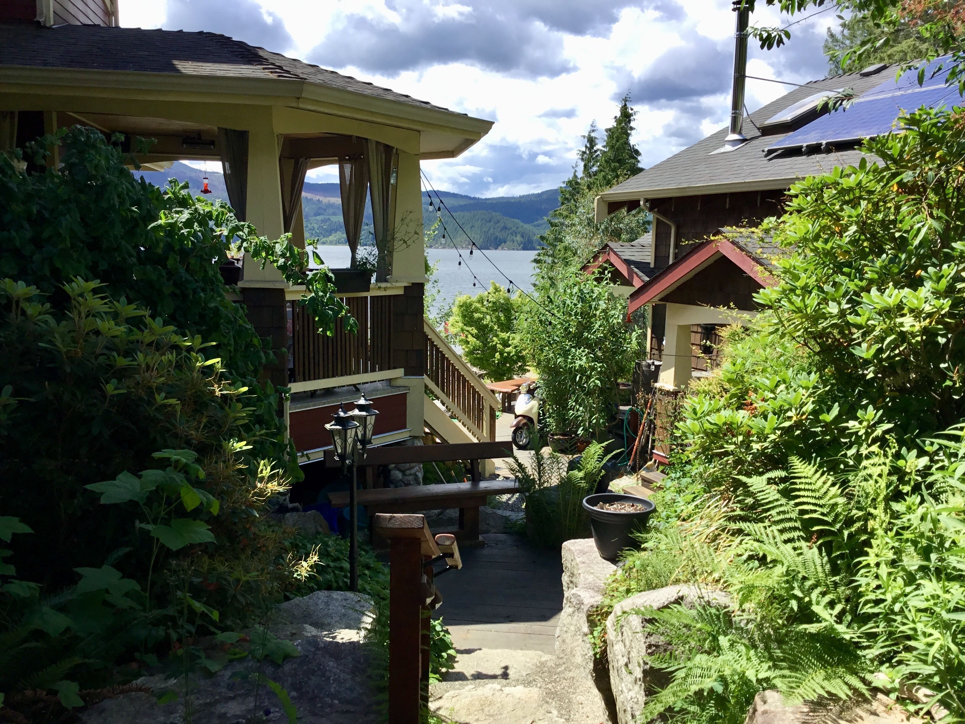 A residential area with a wooden staircase leading to a deck overlooking a body of water, surrounded by lush greenery.