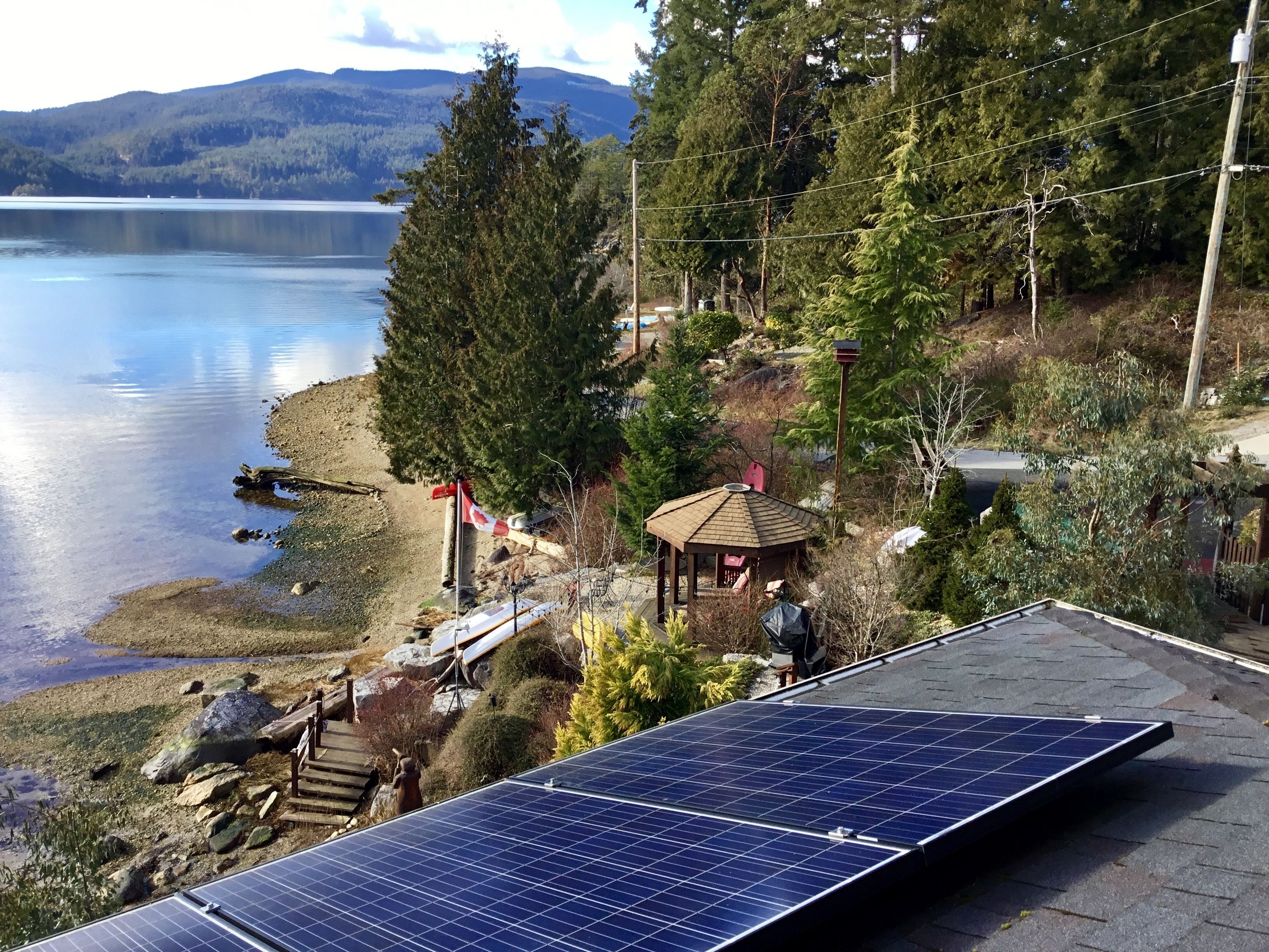 A lakeside property with a gazebo, solar panels, and a view of the lake and mountains.