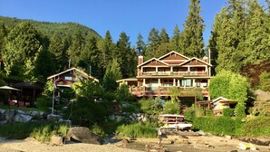 A large lodge with multiple balconies, surrounded by dense forest and a rocky shoreline. - The Tuwanek Hotel and Spa (Sechelt)