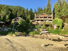 Un gran albergue con varios balcones, rodeado de un bosque frondoso y una costa rocosa.