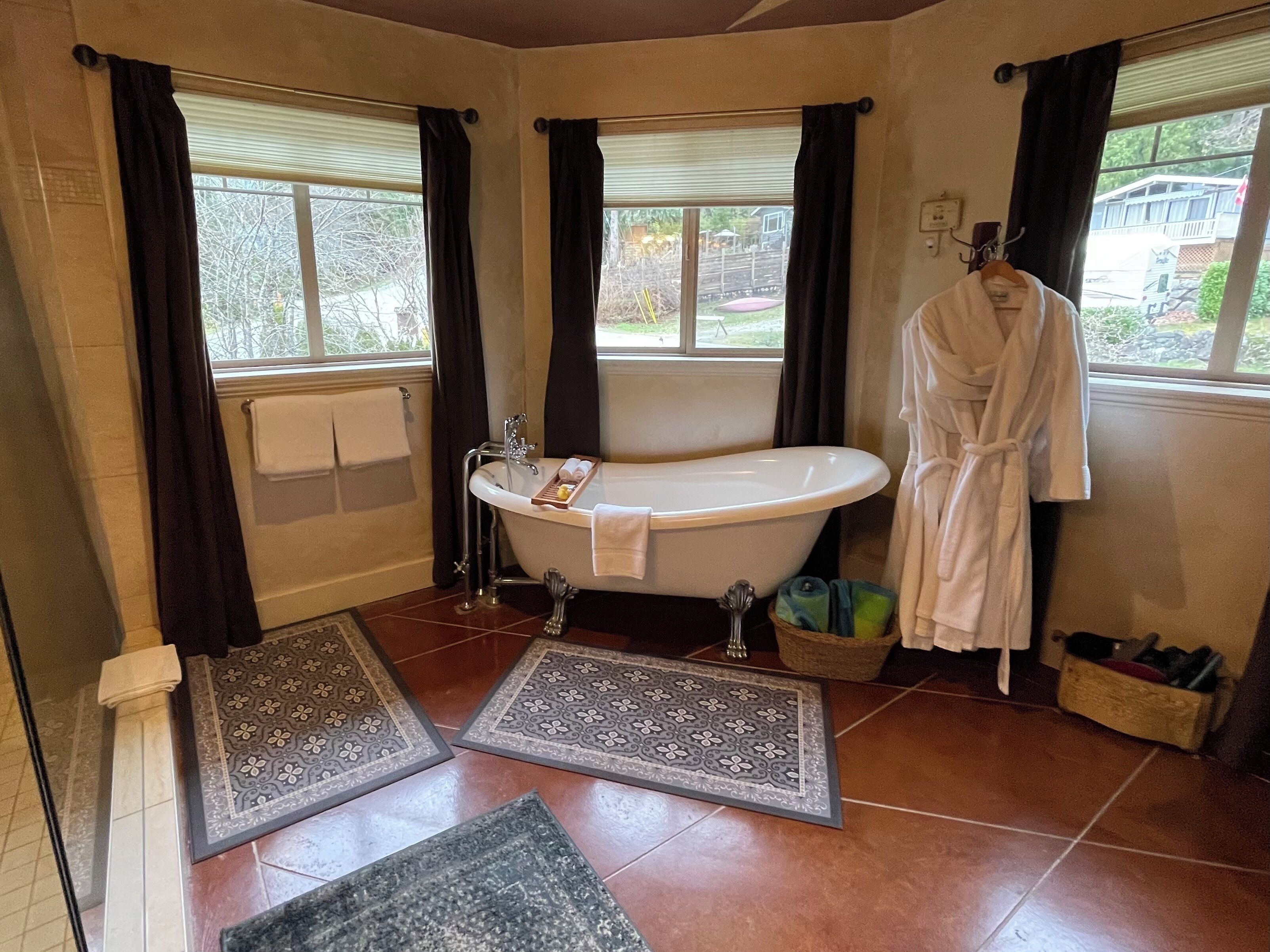 A bathroom with a freestanding bathtub, a towel rack, a robe hanging on the wall, and a window with curtains.