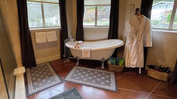 A bathroom with a freestanding bathtub, a towel rack, a robe hanging on the wall, and a window with curtains.