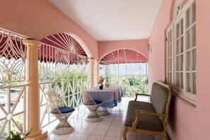 A covered patio with a table and chairs, a sofa, and a view of greenery.