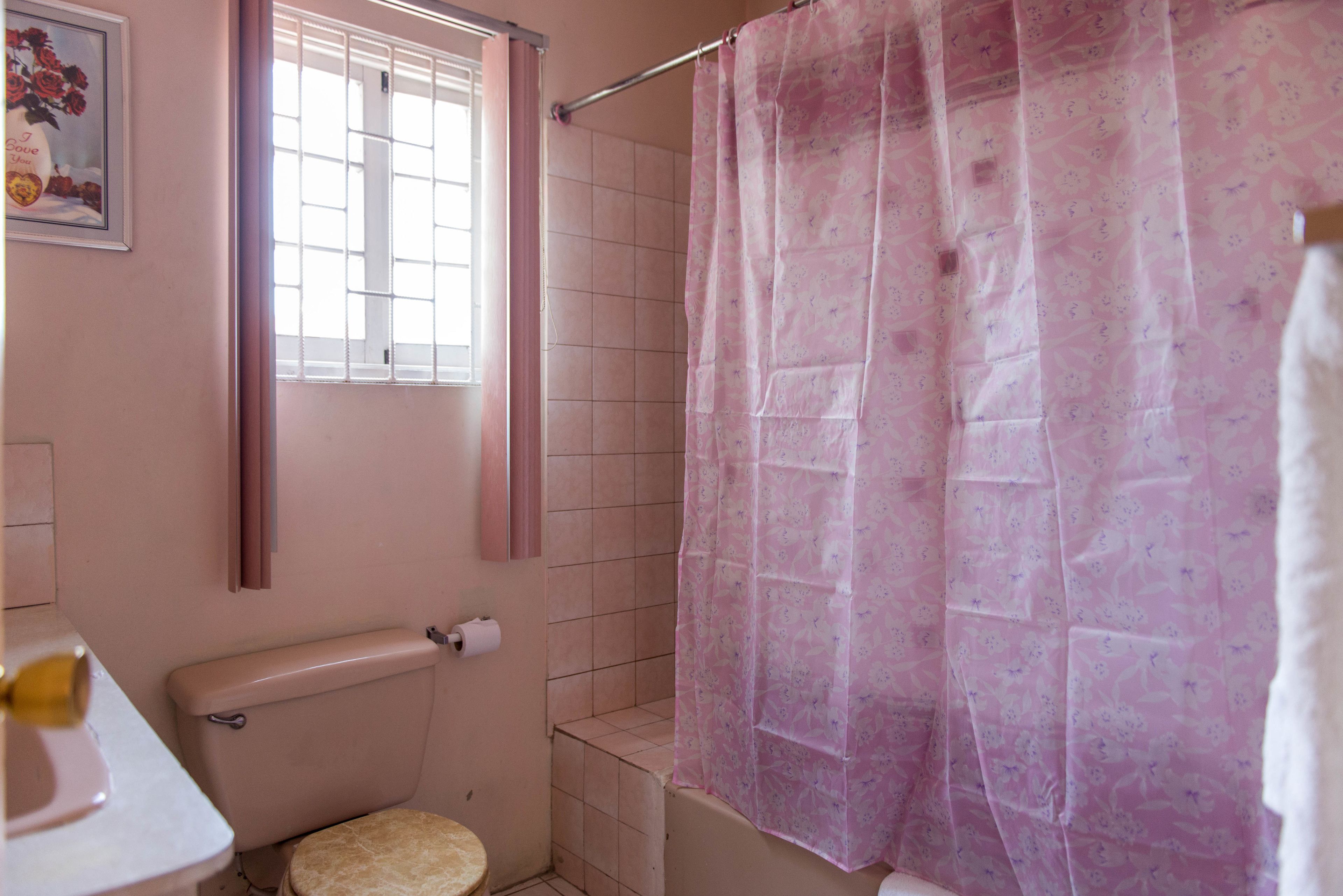 A bathroom with a toilet, a shower curtain, and a window with blinds.