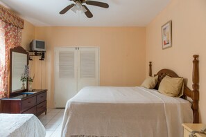 A bedroom with a bed, a dresser, a television on a stand, and a ceiling fan.