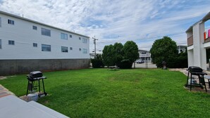A grassy backyard with a barbecue grill, picnic table, and a gas tank. - Flagship Motor Court (Hampton)