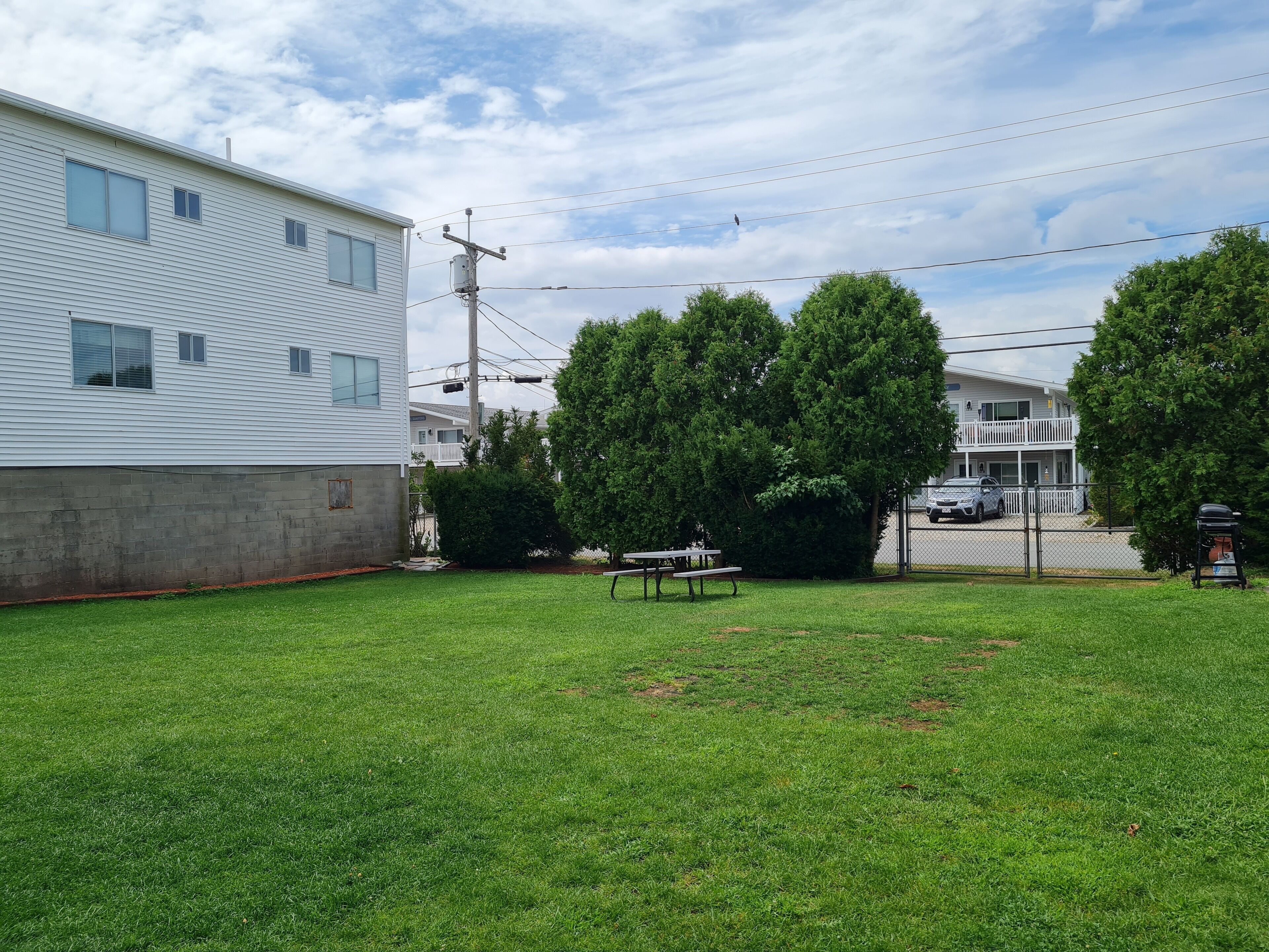 A residential area with a white two-story house, a grassy yard, a picnic table, and a fence.