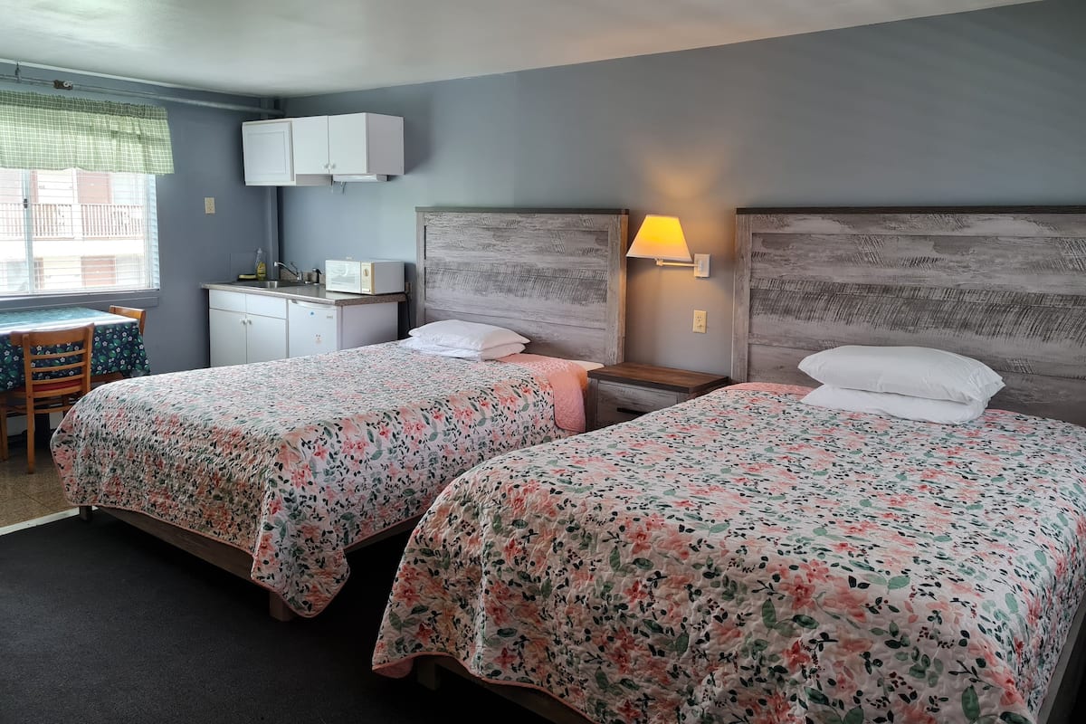 A hotel room with two beds, a small desk, a microwave, and a window with blinds.