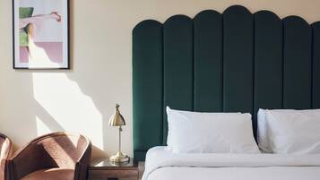 Een net opgemaakt bed met witte lakens, een groen bekleden hoofdeinde en een nachtkastje met een lamp.