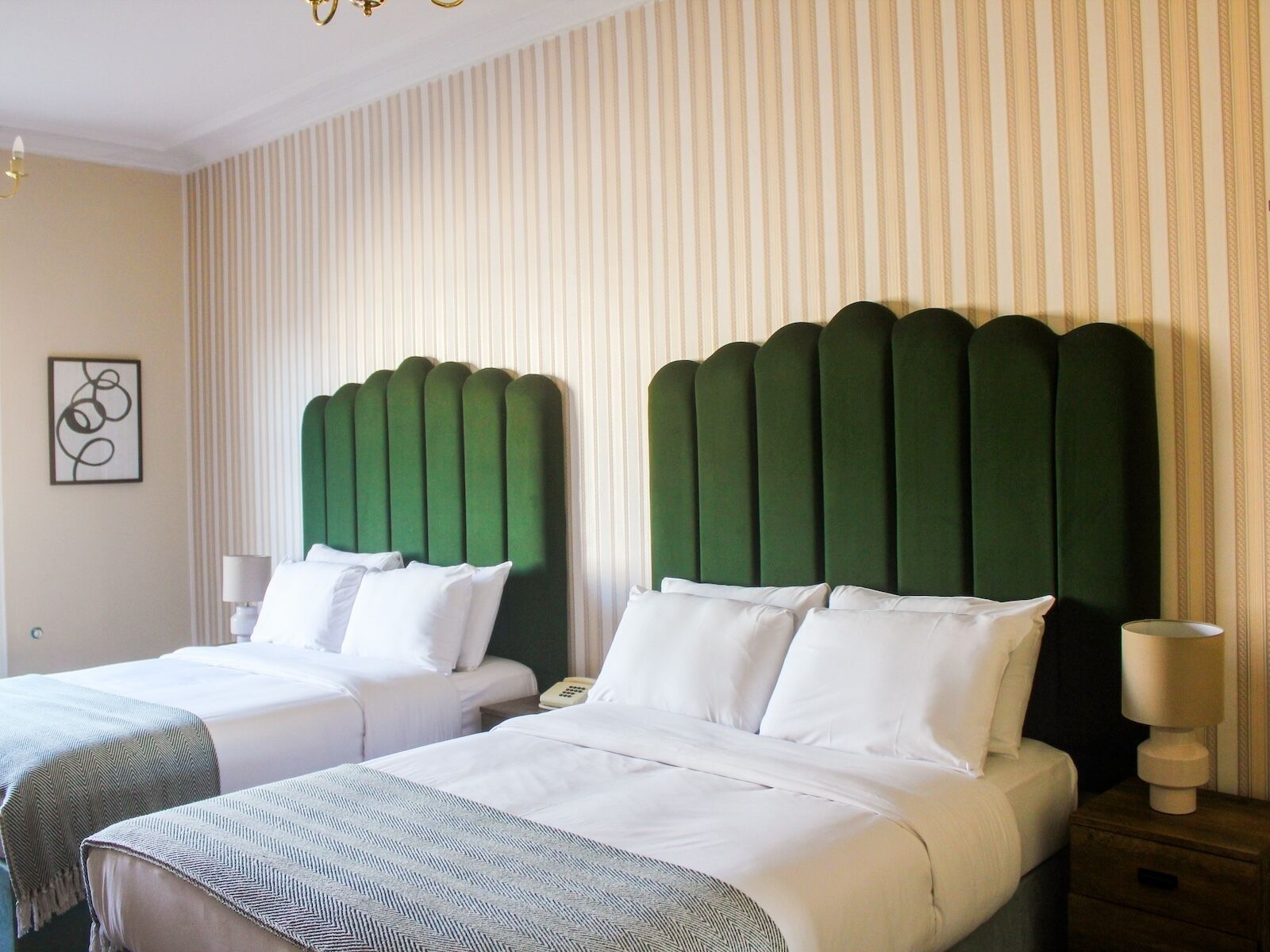 Ein Hotelzimmer mit zwei Betten, jeweils mit einem grünen, gepolsterten Kopfteil, weißer Bettwäsche und einem kleinen Nachttisch mit einer Lampe.