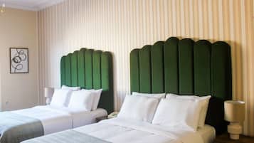 Ein Hotelzimmer mit zwei Betten, jeweils mit einem grünen, gepolsterten Kopfteil, weißer Bettwäsche und einem kleinen Nachttisch mit einer Lampe.