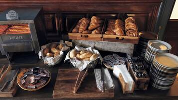 Een bakkerijdisplay met diverse broden en gebak, een broodsnijmachine en een stapel borden.
