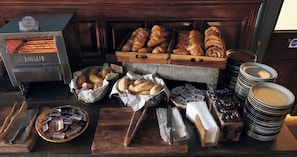 A bakery display with various breads and pastries, a bread slicer, and a stack of plates.