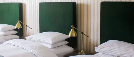 Een hotelkamer met drie bedden, elk met groene hoofdborden en witte beddengoed. Er staan twee nachtlampjes bij elk bed.