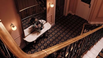Een statige trap met sierlijke balustrades, een spiegel en een bloevas op een bijzettafeltje.