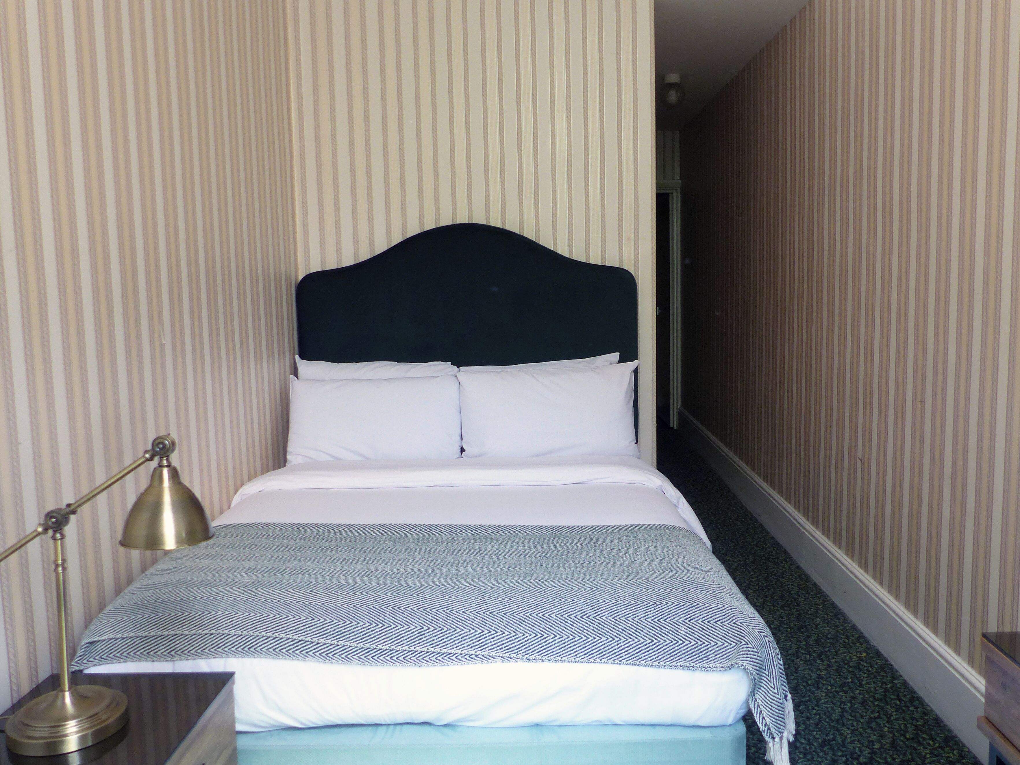 Una habitación de hotel con una cama, una lámpara de noche y papel tapiz a rayas.
