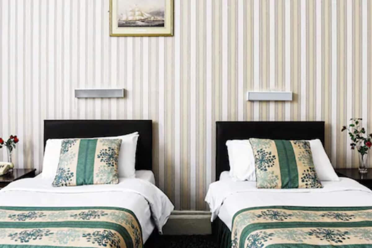 A hotel room with two beds, striped wallpaper, a framed picture on the wall, and a nightstand with a vase of flowers.