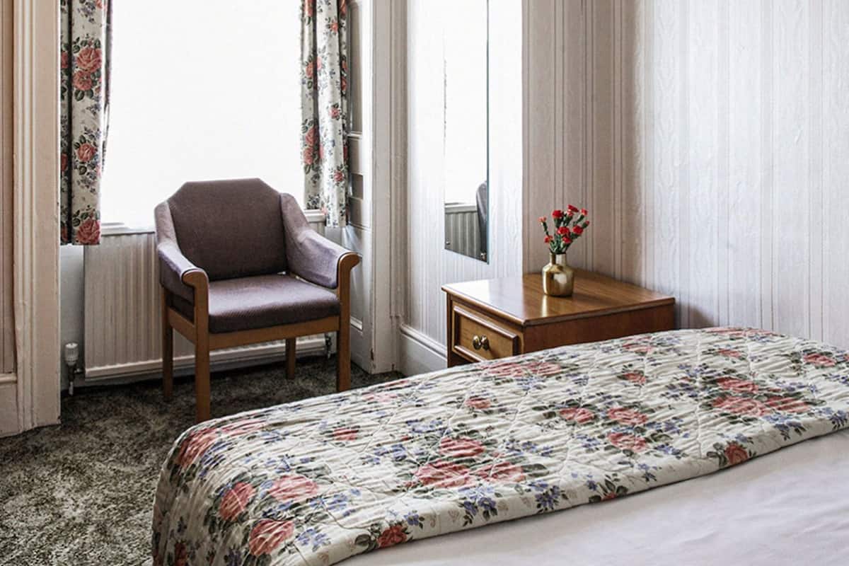 A hotel room with a bed, a chair, a dresser, and a window with curtains.