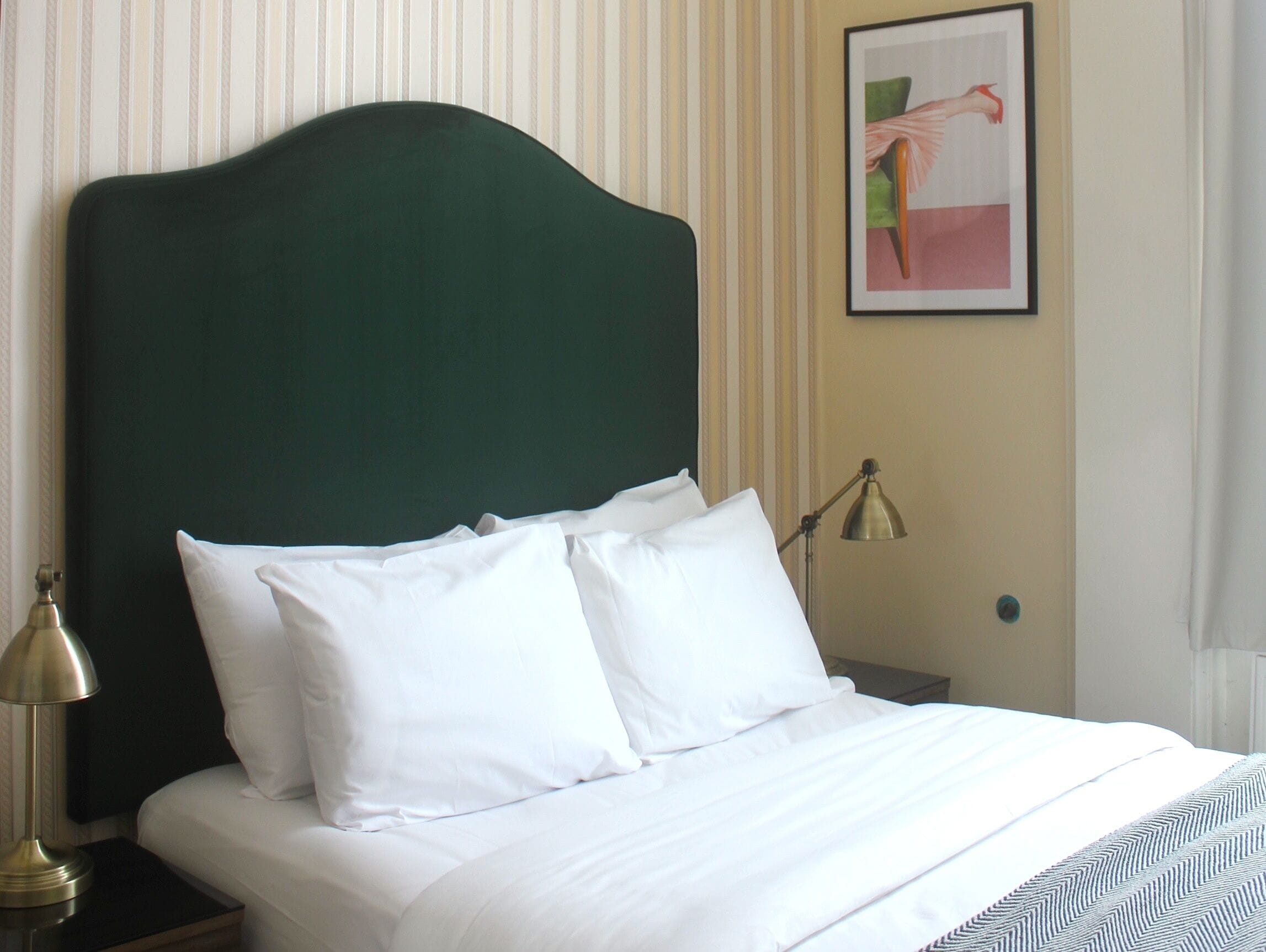 A neatly made bed with white linens and a green upholstered headboard.