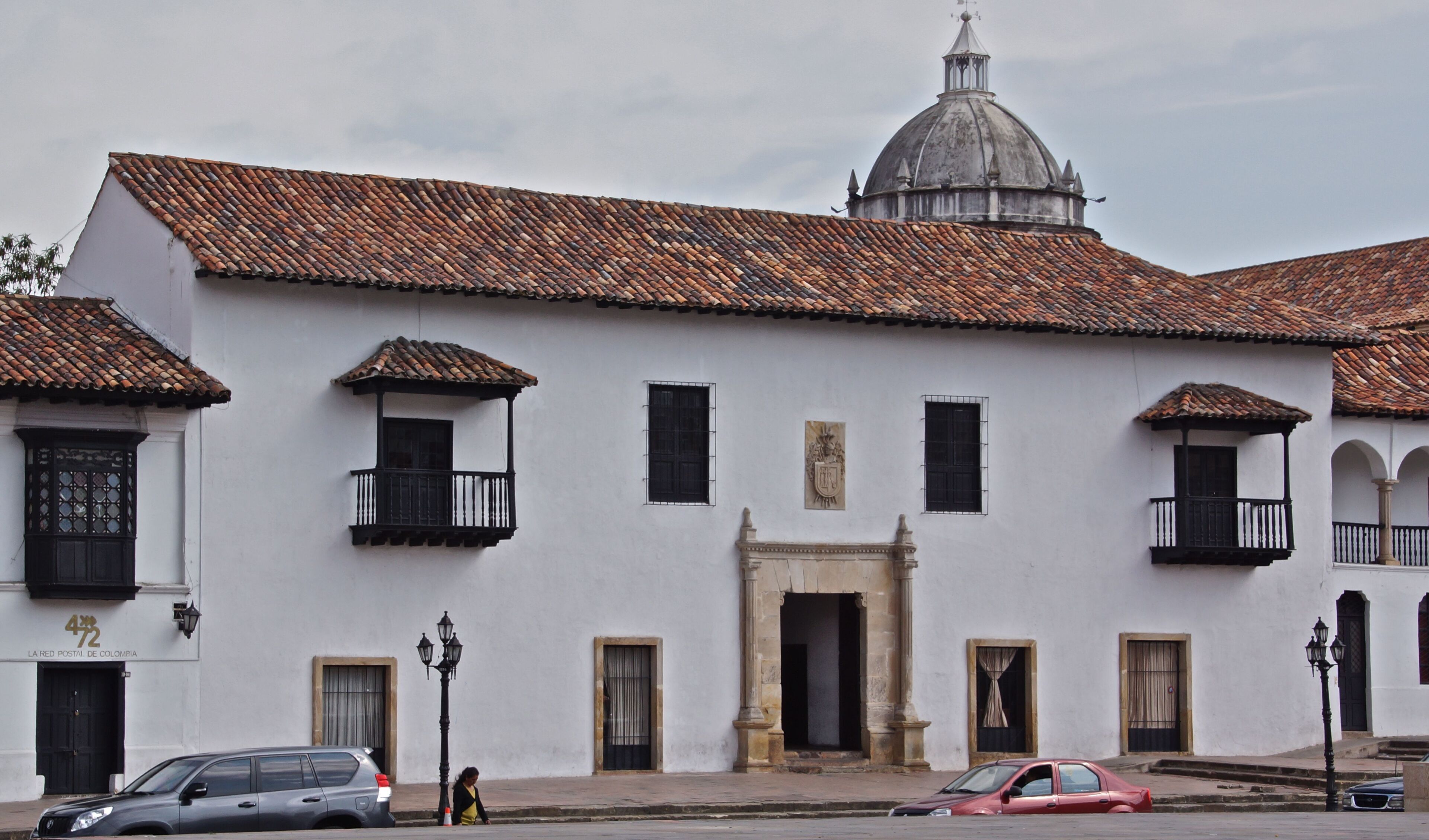 A white colonial-style building with a tiled roof, multiple balconies, and a central entrance.