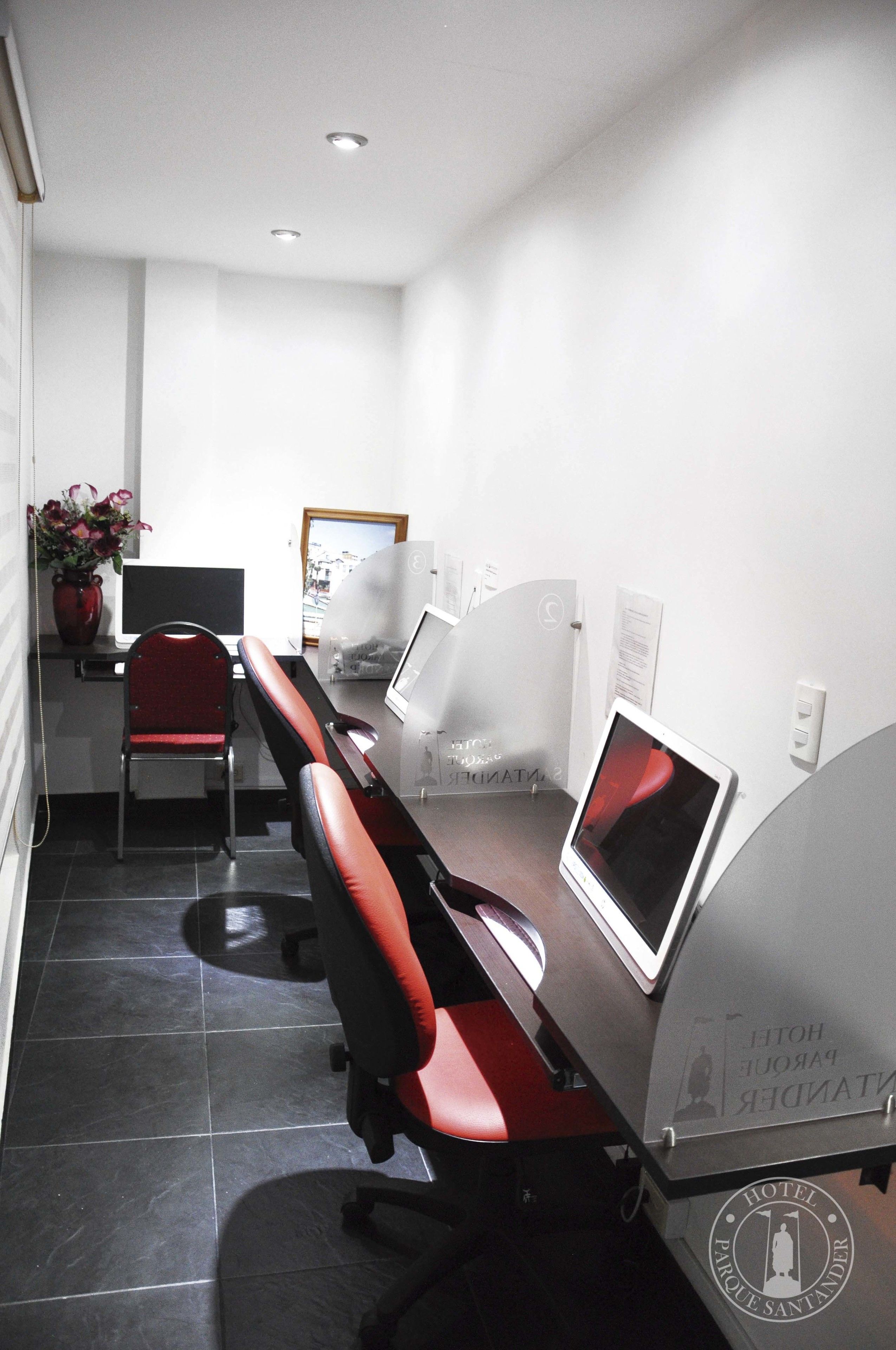 A conference room with a long table, red chairs, and two computer monitors.