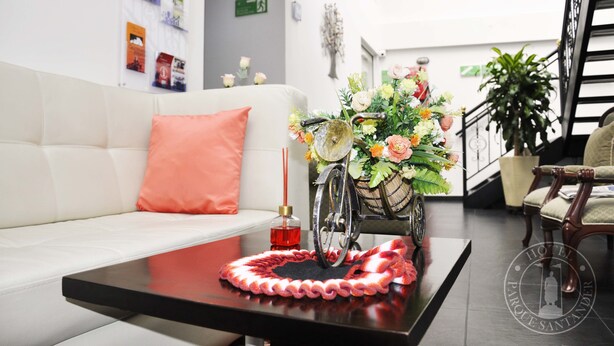 A modern hotel lobby with a white sofa, a decorative flower arrangement on a vintage bicycle, and a red candle on a black table.