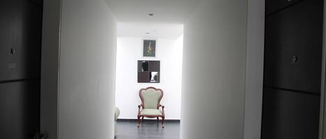 A hallway with a chair, doors, and a framed picture on the wall.