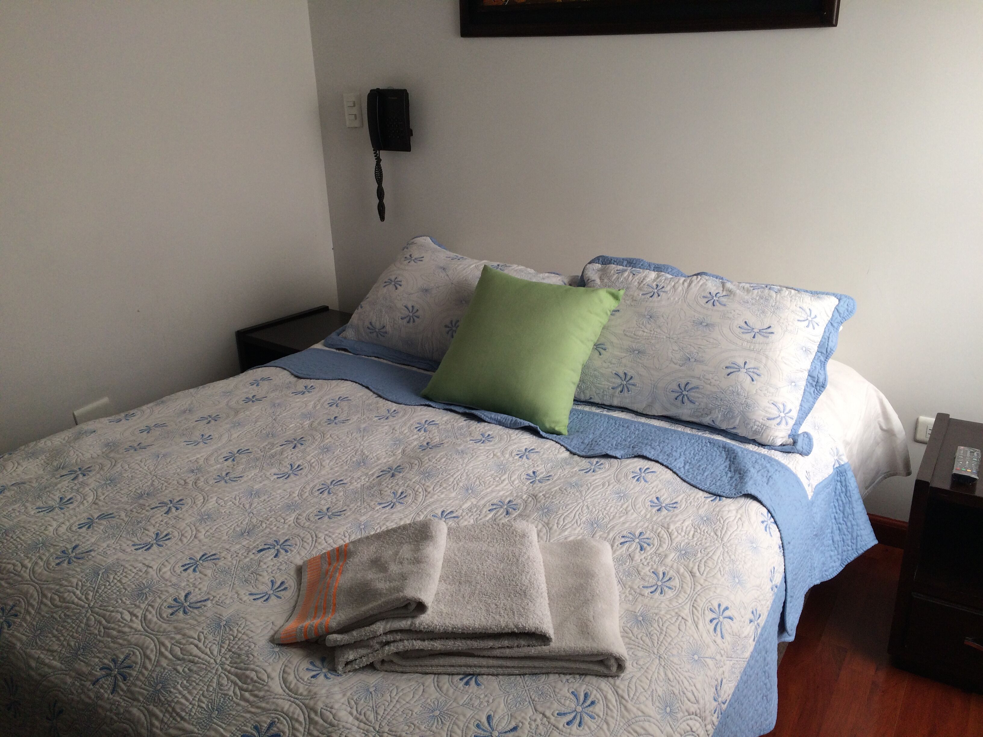 A neatly made bed with a floral patterned bedspread, a green pillow, and a folded towel on the bed.
